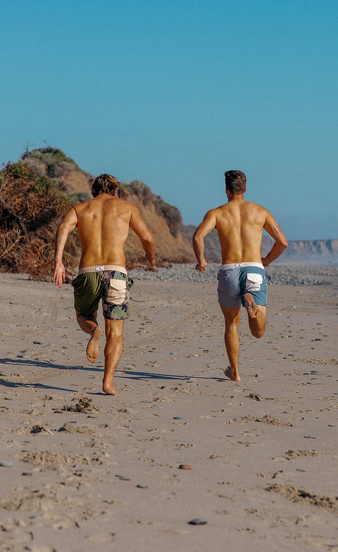Two men running on the beach wearing the wright shorts in army/camo and quarry/slate.