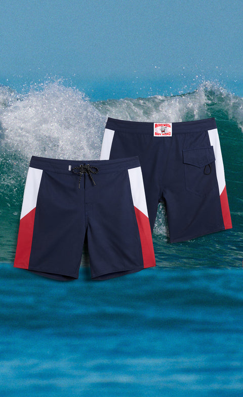 The Patriot Birdie Boardshort. Featuring Navy fabric with side panels with white and red. Two images of the boardshorts over a background image of the ocean.