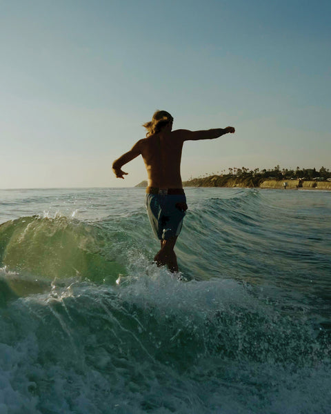 Joel Tudor walks toward the nose of his blue longboard while surfing, arms out for balance, wearing Birdwell 300 Legend boardshorts.