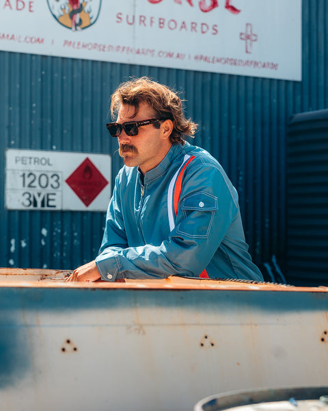 Kevin Skvarna is leaning over a blue and tan vintage truck wearing the Birdwell Racing Jacket 25 in Le mans/Federal Blue. The jacket is made from SurfNyl® material in federal blue jacket with vertical stripes - one blue, one orange. 