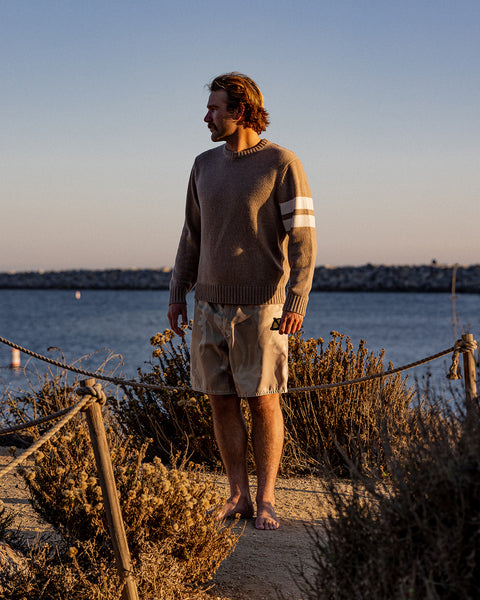 Kevin standing by a body of water at sunset, wearing a comp stripe sweater and shorts.