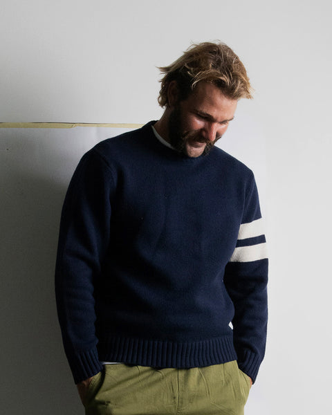 Kevin wearing a navy sweater with white stripes on a plain background