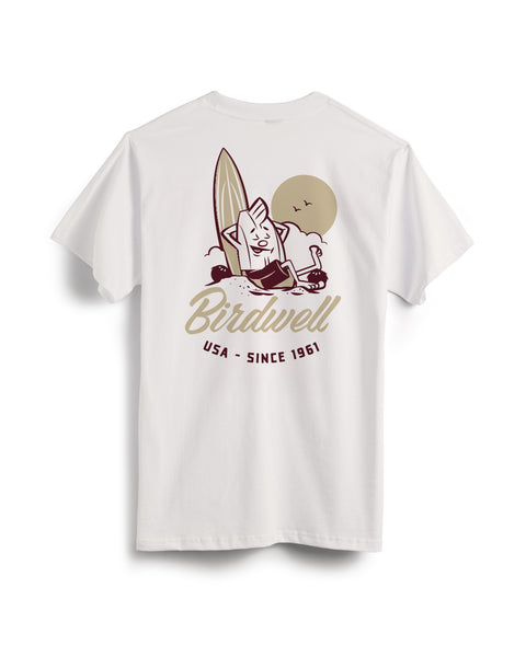 Back View of Vintage White T-shirt with a graphic design on the back featuring a Birdie leaning against a surfboard with his foot up on a coconut and text below of Birdwell USA Since 1961. Product on a white background.
