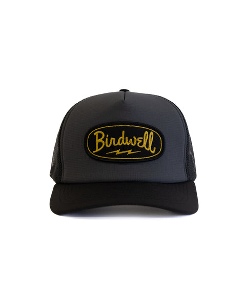 Black and grey hat with BIRDWELL yellow logo on the front with a white background