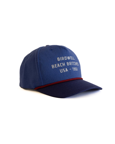 'Birdwell Beach Britches USA - 1961' in white text on blue hat with a dark navy rim and red string over brim with text on a white background