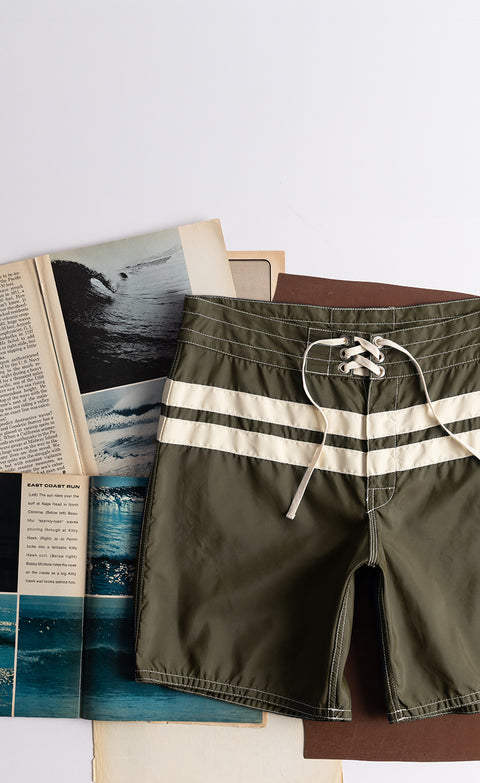 Dark Olive Boardshorts with Bone Stripes over background with vintage surf magazines.
