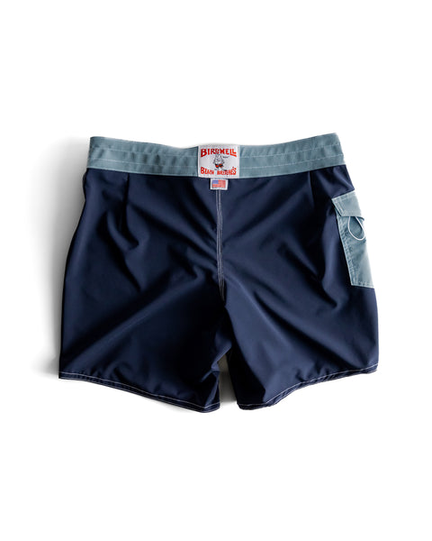 Back view of the 806 boardshorts, navy body with federal blue waistband and pocket. White License plate label with Made in USA Label beneath. Product on white background.