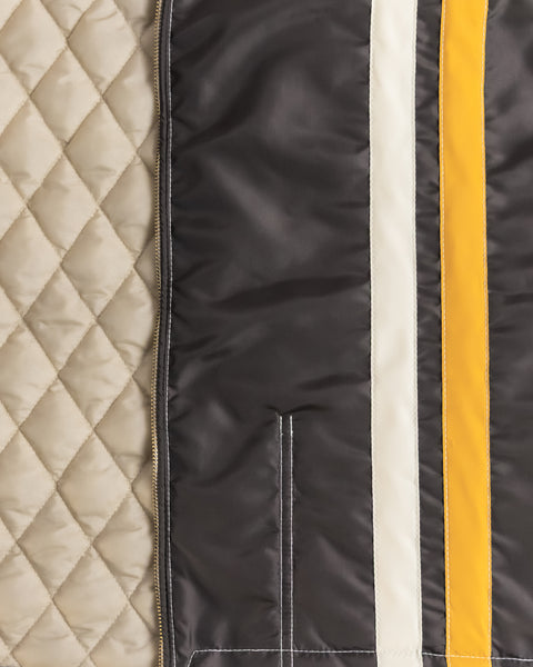 Close-up of the Birdwell Quilted Racing jacket half interior of the quilt with the talon zipper and diamond pattern. The other half is the outside of the jacket with the pleats in white, white vertical stripe and yellow vertical stripe. 