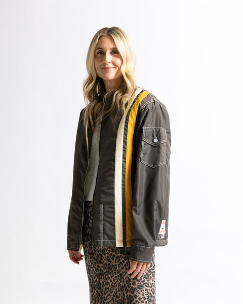 Model wearing the Birdwell Quilted Racing SurfNyl®  in brown with yellow and white stripes, with a brand logo on the bottom left hem, with a button pocket closure on the left arm in front of a white background