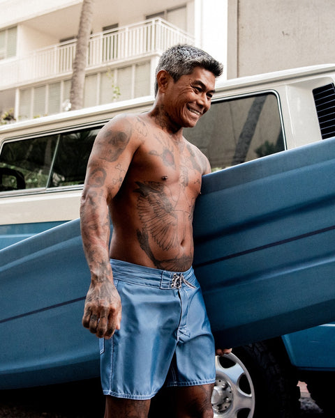 Man with tattoos holding a blue surfboard next to a white van