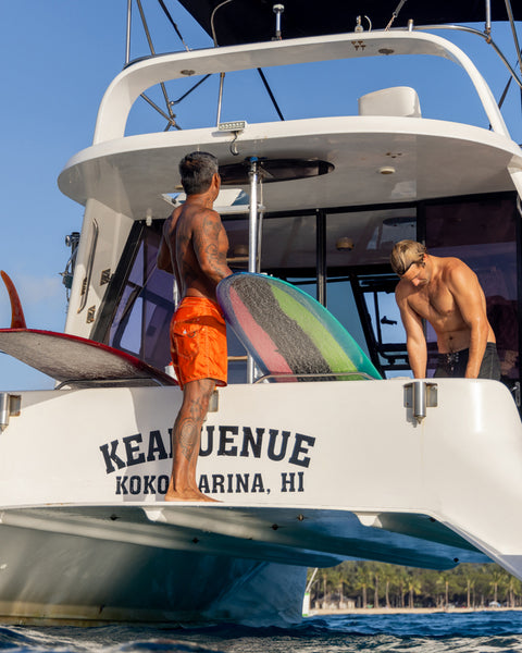 Two men on a boat with a rainbow surfboard, docked at Kona Venue in Koko Head, Hawaii.