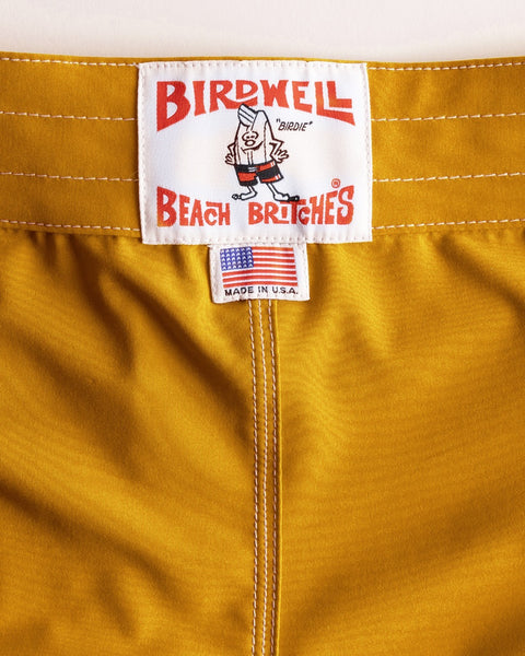 Close-up of a label on mustard yellow shorts with 'Birdwell Beach Brictches' branding.
