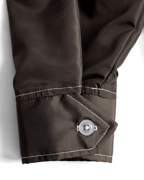 A close-up of the Racing Jacket 26 - Brown/Bone/Gold cuff shows dark fabric with white stitching, a single button, and an angular design, set against a white background.