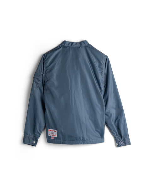 The Racing Jacket 26 in Federal Blue/White/Orange is shown from the back, laid flat on a white background. It features a vintage-inspired style, a left hem patch with text and graphics, and an upper right sleeve pocket. Made in America.