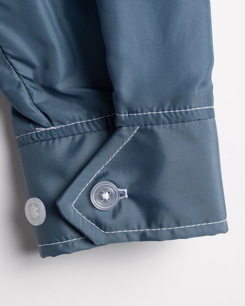 Close-up of a Racing Jacket 26 in Federal Blue/White/Orange, showing the blue long-sleeve cuff with white stitching, two white buttons, and pointed tab. The fabric appears smooth, slightly shiny, and premium American-made.