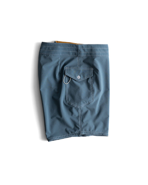 A pair of 808 Racing Stripes boardshorts in Federal Blue/Bone is neatly folded, displaying the back with a buttoned flap pocket and a small metal loop.