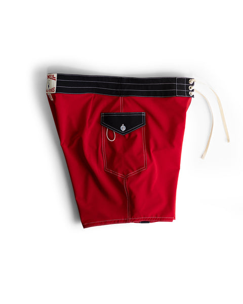 808 Mono Stripe - Red/Black boardshort features a red body, black waistband, white drawstring and stitching, plus medium-length fit. Includes a back pocket with flap, loop, and button closure. Photographed flat on a white background.