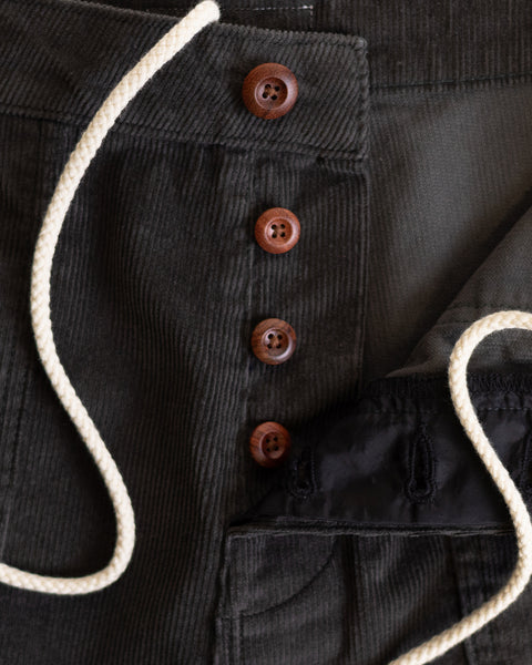 Close-up of Classic Corduroy Shorts - Oregano in dark green corduroy, showing four brown buttons, partially unbuttoned to reveal the inside pocket lining and an adjustable drawcord waist draped across the fabric.