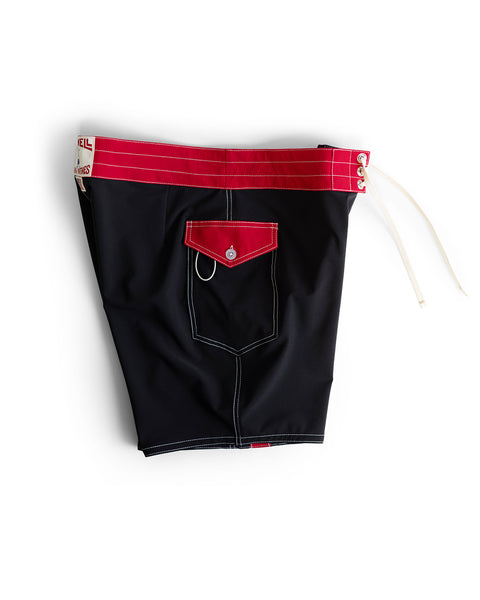 808 Mono Stripe - Black/Red boardshorts featuring a bold red waistband, white drawstrings, and a small red flap pocket with metal grommet. Medium-length and made in the USA. Displayed on a white background.