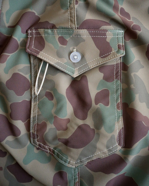 A close-up of the 808 SurfStretch Side Pocket Boardshorts in Frogskin Camo, highlighting the flap pocket with button closure and a white plastic cable partially tucked inside.