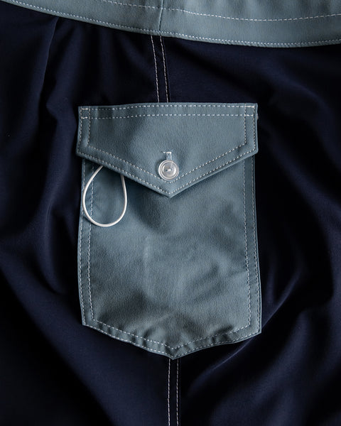 Close-up of the 808 Pop Pocket - Navy/Federal Blue shows a blue buttoned pocket with white stitching and a white wire around the button, crafted from SurfStretch® boardshort material and proudly made in the USA.