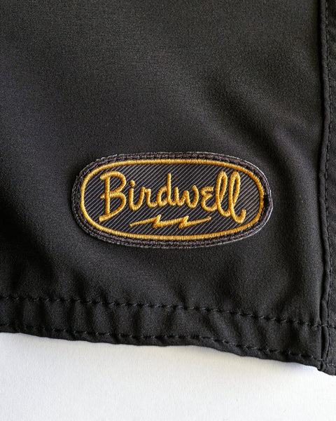 Close-up of the 808 Powerbird - Black boardshort, featuring a stitched seam and an oval embroidered 