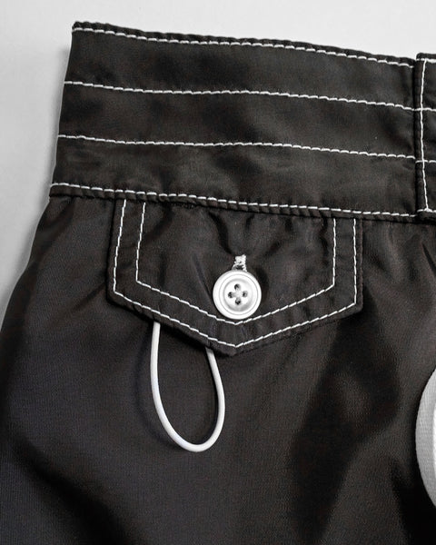 Close-up of the 400 Boardshorts - Black shows a black fabric waistband with white stitching, a buttoned flap pocket, and a small white loop under the pocket designed for quick-drying convenience.