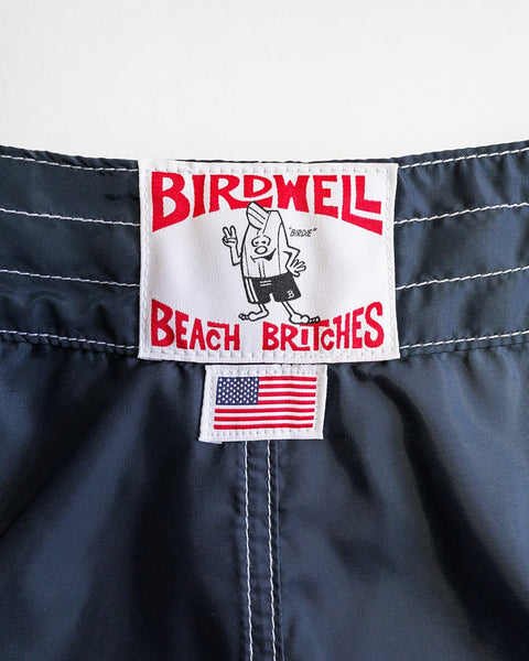 Close-up of the waistband label on navy 400 Boardshorts, featuring a red Birdwell Beach Britches logo with a cartoon bird in swimwear and a small 