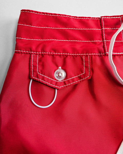 Close-up of the waistband and pocket of 400 Boardshorts - Red, featuring white stitching, a clear button on the pocket flap, and a white elastic loop on the waistband.