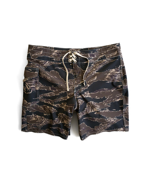The 808 SurfStretch Side Pocket Boardshorts - Tiger Camo are medium-length boardshorts with a brown, black, and beige tiger stripe camo pattern, a white front drawstring, and a side pocket, shown on a white background.
