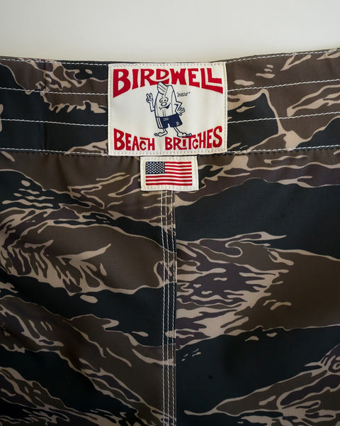 Close-up of 808 SurfStretch Side Pocket Boardshorts in Tiger Camo, showcasing a Birdwell Beach Britches label and an American flag patch below the waistband—expertly made in the USA.
