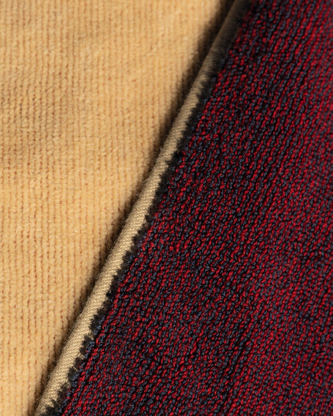 Close-up of the License Plate Towel - Bone: a tan, ribbed 100% cotton fabric overlapping diagonally with another dark red fabric featuring a black and blue woven pattern.