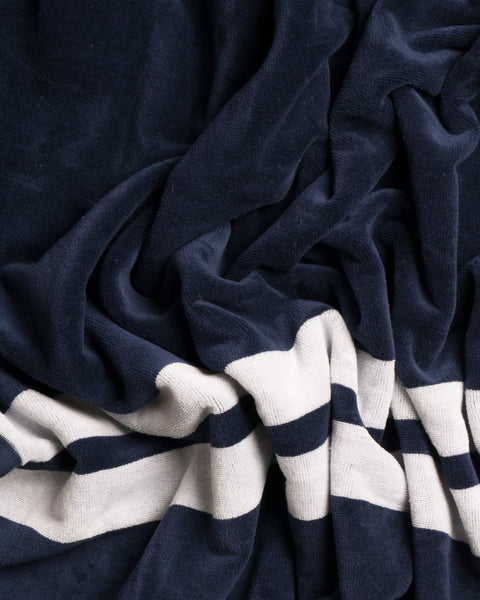 A close-up of the Comp Stripe Towel - Navy/White, made in USA, showcases its soft, plush texture and oversized design with navy fabric accented by white and navy horizontal stripes near the bottom.