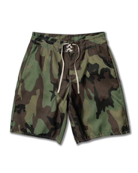 The 312 Boardshorts - Woodland Camo feature a green and brown camo pattern, white drawstring, and visible stitching, displayed flat on a white background. Made in USA.