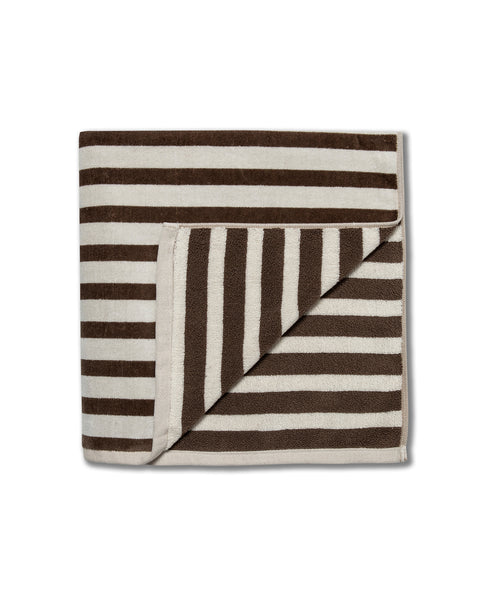 The Beach Towel - Vintage White/Brown is an oversized cotton towel with brown and cream stripes, one corner folded to reveal the reverse. Proudly made in the USA, this limited edition piece is displayed on a white background.