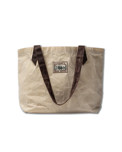The Beach Tote - Natural is a beige waxed cotton canvas bag with dark brown handles and a rectangular BIRKENSTOCK 1774 EVAS BOTTLES patch. From the Elwood collaboration, its wrinkled design is shown against a white background.