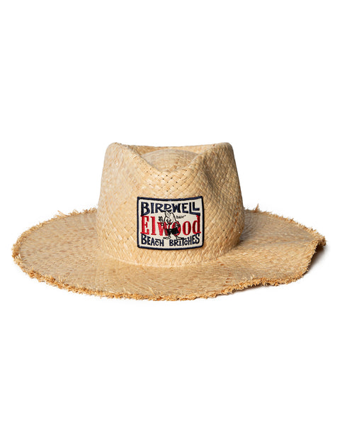 The Straw Hat - Natural is a wide-brimmed straw hat with a raw edge. It has a front rectangular patch reading BIRDWELL x Elwood BEACH BRITCHES in black and red, plus a small embroidered bird.