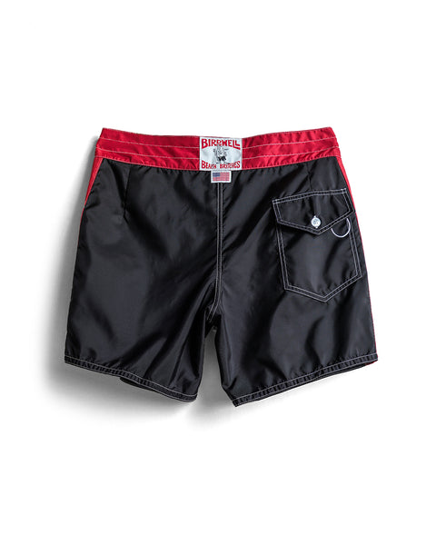 The 310 Dekka - Black/Red boardshorts feature a red waistband and trim, a back pocket with flap and button, and the Birdwell label on the waistband. Made in USA, shown laid flat on a white background.