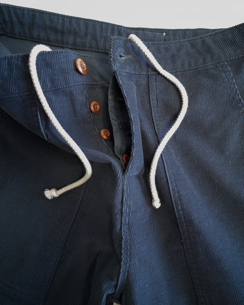 Classic Corduroy Pants - Navy, crafted from navy blue corduroy with white drawstrings and brown buttons, featuring a partial SurfNyl fly and Birdwell-inspired accents, are shown partially unbuttoned and open at the waistband, lying flat on a light surface.
