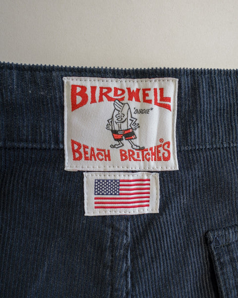 A close-up of the Classic Corduroy Pants - Navy reveals a “Birdwell Beach Britches” label featuring a cartoon bird and a small American flag patch below, showcasing classic details such as the signature SurfNyl fly for enhanced durability.