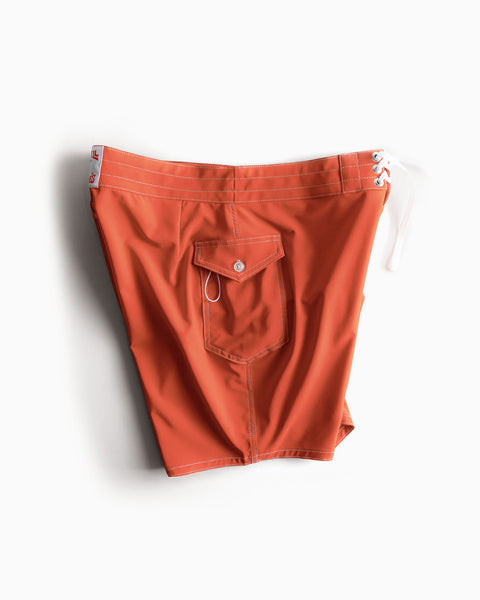 The 808 SurfStretch Side Pocket Boardshorts in Paprika feature a medium-length orange design with white stitching, a back pocket, and a white drawstring at the waistband. These boardshorts are displayed against a plain white background.