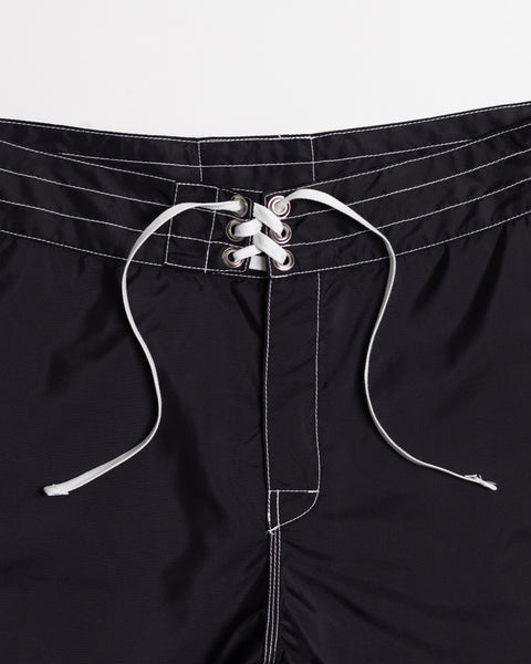 Close-up of the waistband of the 312 Boardshorts - Black, featuring a white lace-up drawstring threaded through metal eyelets and white stitching detail. These long-length boardshorts are proudly made in the USA.