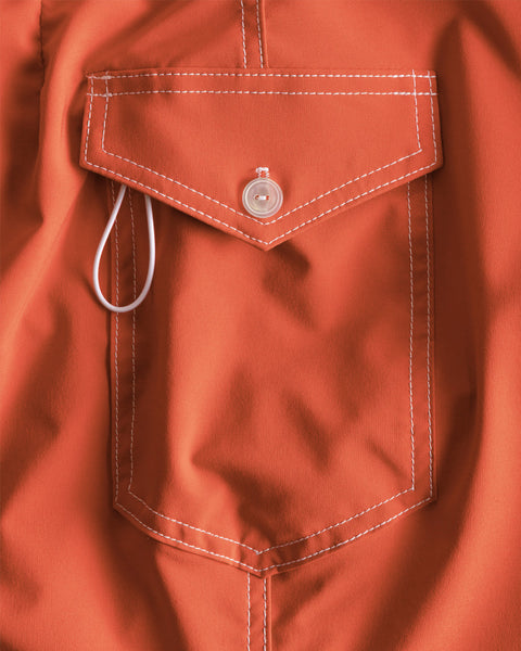 Close-up of the 806 SurfStretch Side Pocket Boardshorts in Paprika, featuring an orange fabric pocket with white stitching, a flap secured by a white button, and a white loop peeking from under the flap—expertly crafted in the USA from innovative SurfStretch® material for ultimate comfort and performance.