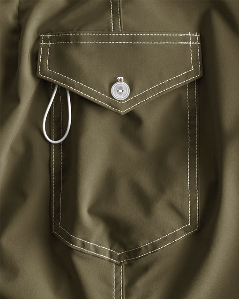 Close-up of the side pocket on the 806 SurfStretch Side Pocket Boardshorts in Dark Olive, featuring white stitching, a silver button closure, and a white looped cord partially visible on the left side of the pocket flap. Made in the USA from premium SurfStretch material for optimal comfort and flexibility, this detail highlights quality construction.