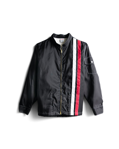 Racing Jacket 26 - Black/White/Red is a vintage-inspired black racing jacket with a zip front, featuring one red and one white diagonal stripe on the left side. It includes a small pocket with a button on the left sleeve and has a collarless neckline.