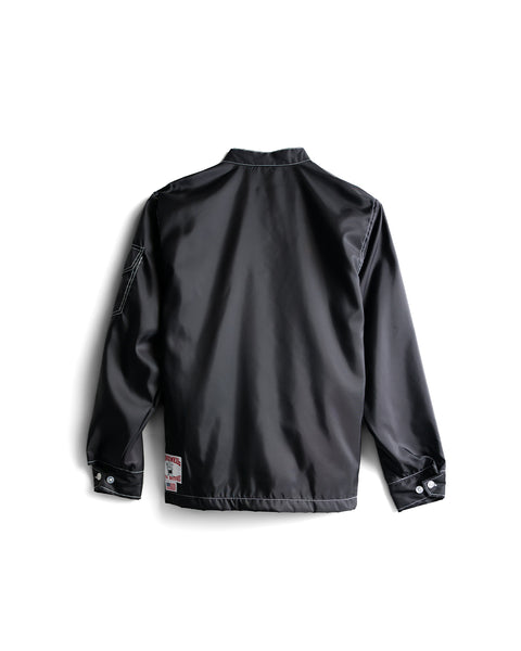 The Racing Jacket 26 in Black/White/Red is shown from the back, featuring a collar, long sleeves with buttoned cuffs, and a small patch near the bottom hem. Crafted in an American-made tradition, this jacket offers a sleek, smooth texture and a minimalist modern design.