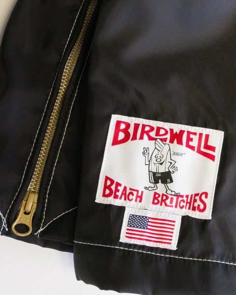 A close-up of the Racing Jacket 26 in black, white, and red—a vintage-inspired, American-made jacket featuring a gold zipper and a patch that reads “Birdwell Beach Britches” with a cartoon bird and a small American flag underneath.
