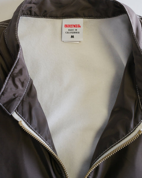 A close-up of the Racing Jacket 26 - Brown/Bone features its dark brown SurfNyl fabric and contrasting white lining, unzipped to reveal the Birdwell Made in California M label inside the collar—crafted from iconic American-made Birdwell SurfNyl material.
