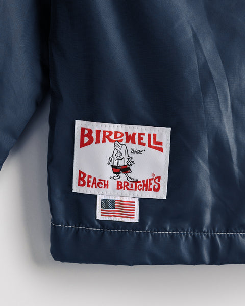 A patch on the navy Racing Jacket 26 - Navy/Bone/Red reads BIRDWELL BEACH BRITCHES with a cartoon character, and is paired with a U.S. flag patch below it, capturing the spirit of this American-made, vintage-inspired racing jacket.