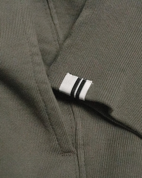 A close-up of dark olive ribbed fabric, crafted from soft French terry, with a small white tag featuring two black stripes sewn into a seam—exemplifying the attention to detail of the Harmony Hoodie - Dark Olive, a premium hoodie made in USA.